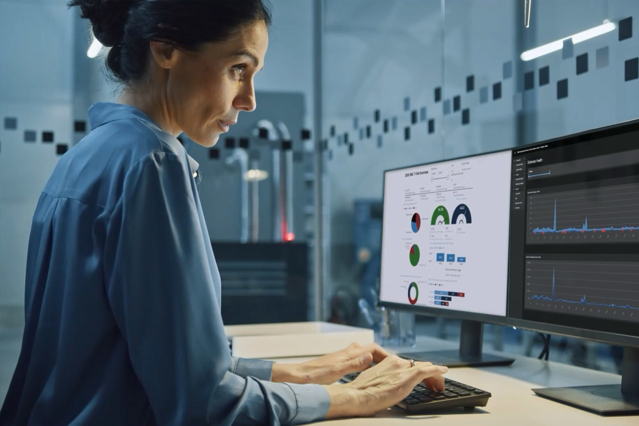 A dark haired woman standing at a desk while typing on a computer.